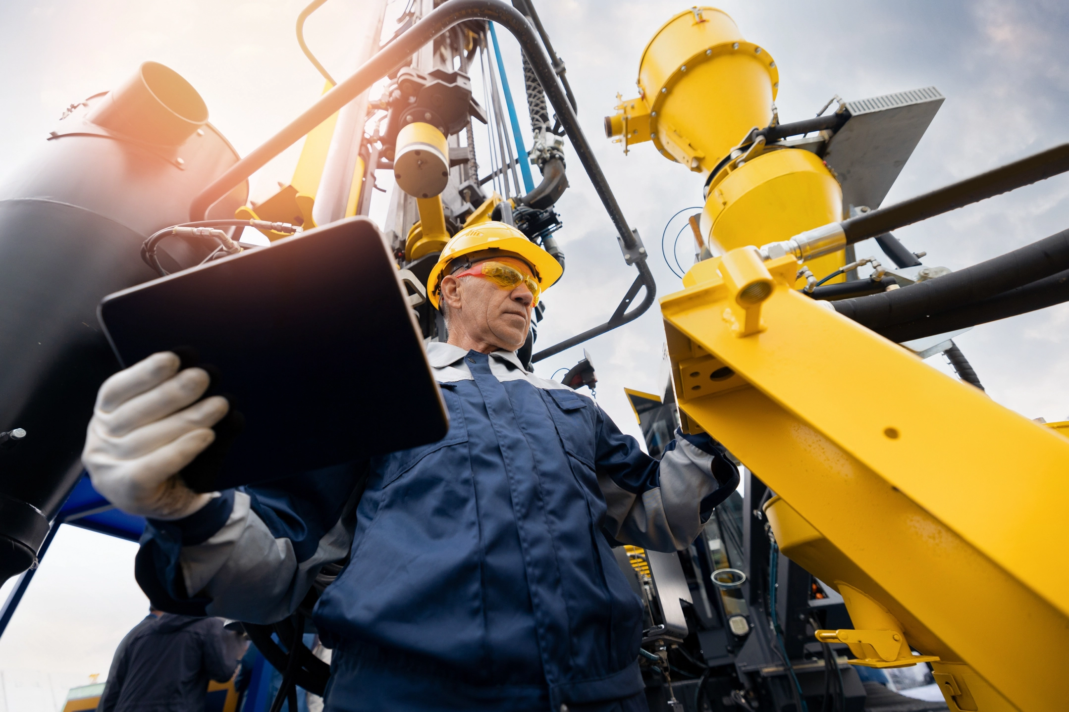 Worker in a hard hat using a tablet beside industrial machinery